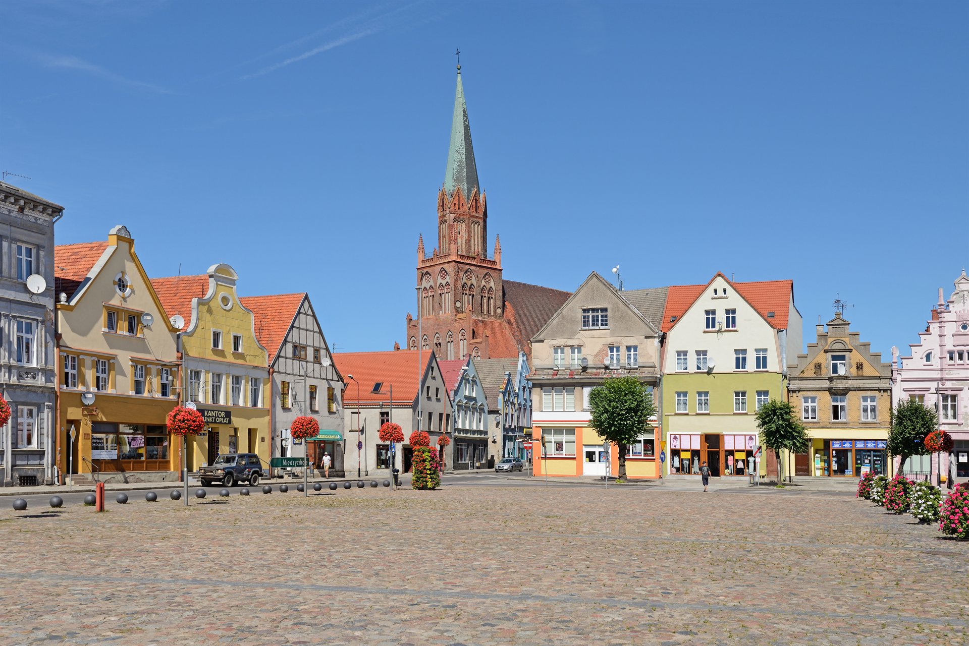 Kolorowe kamienice na rynku i gotycki kościół z wysoką wieżą pod błękitnym niebem