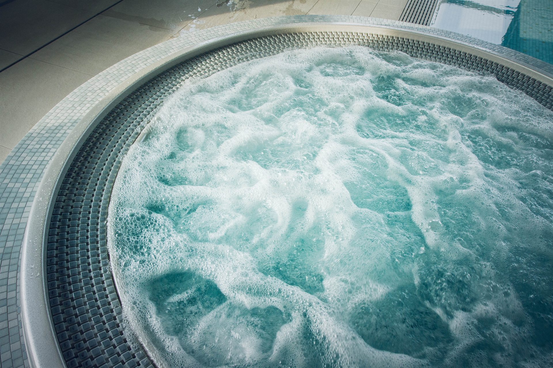 Pieniący się błękitny jacuzzi z okrągłym brzegiem i kafelkami wokół