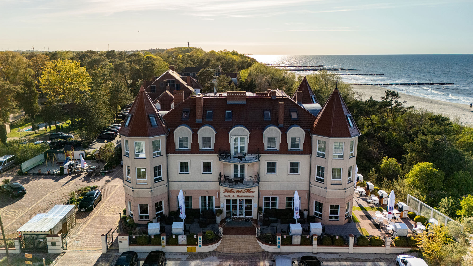 Hotel z wieżyczkami nad morzem, otoczony drzewami, z tarasem i plażą w tle
