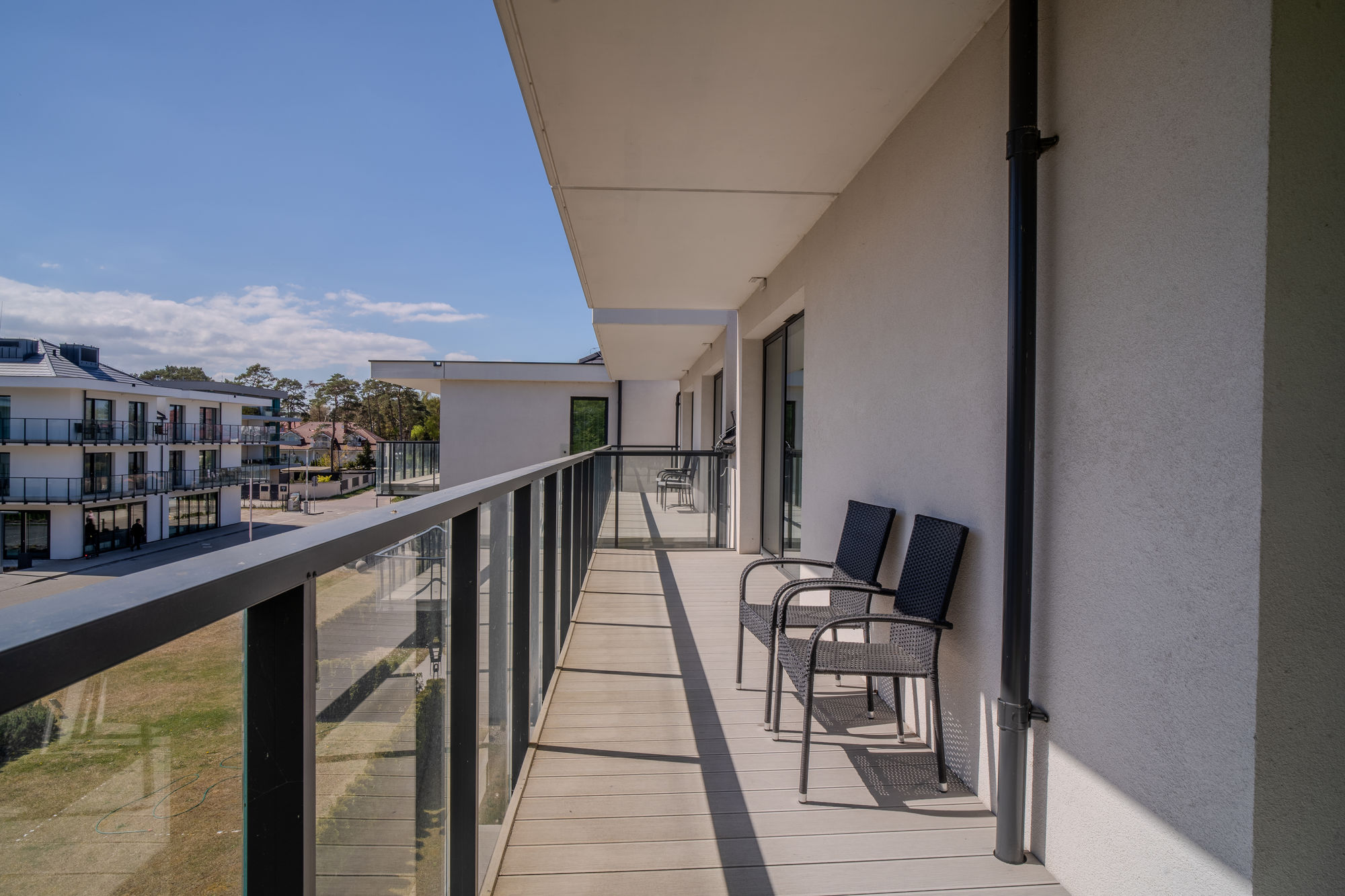 Balkon nowoczesnego budynku z dwoma krzesłami i widokiem na osiedle oraz błękitne niebo