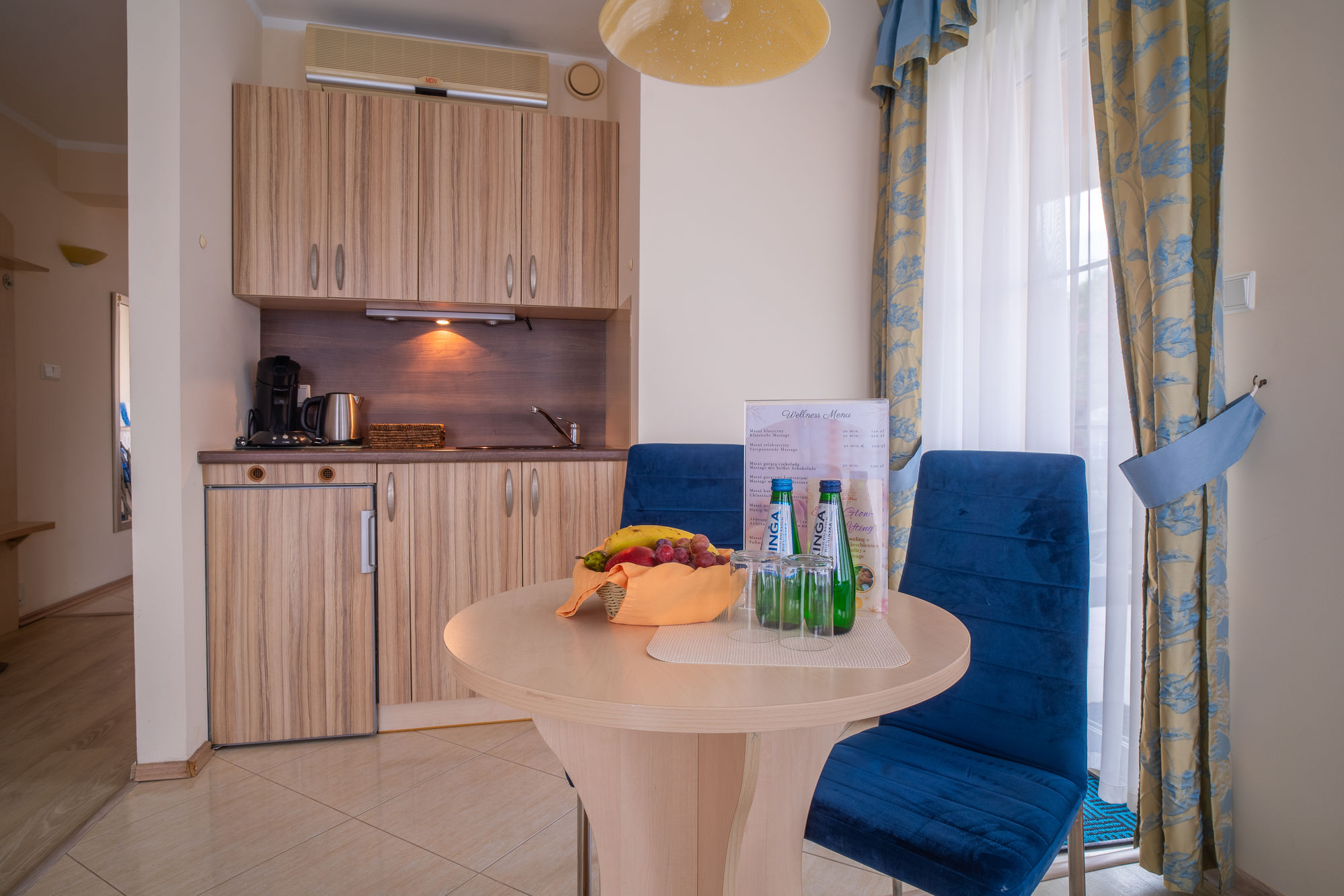Jasny aneks kuchenny z okrągłym stołem, owocami i butelkami przy niebieskich krzesłach