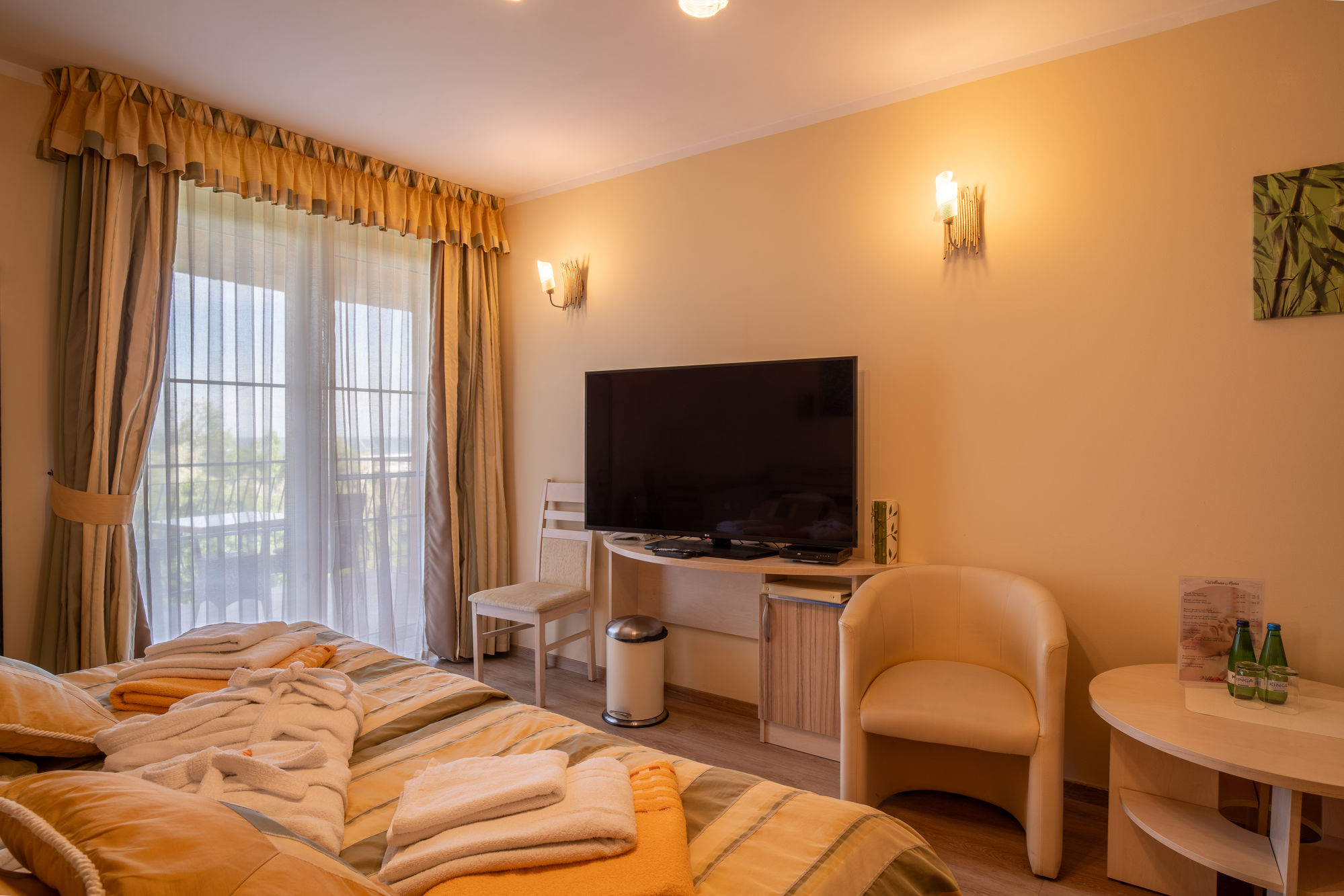 Przytulny hotelowy pokój z łóżkiem, telewizorem, fotelami i balkonem z zasłonami