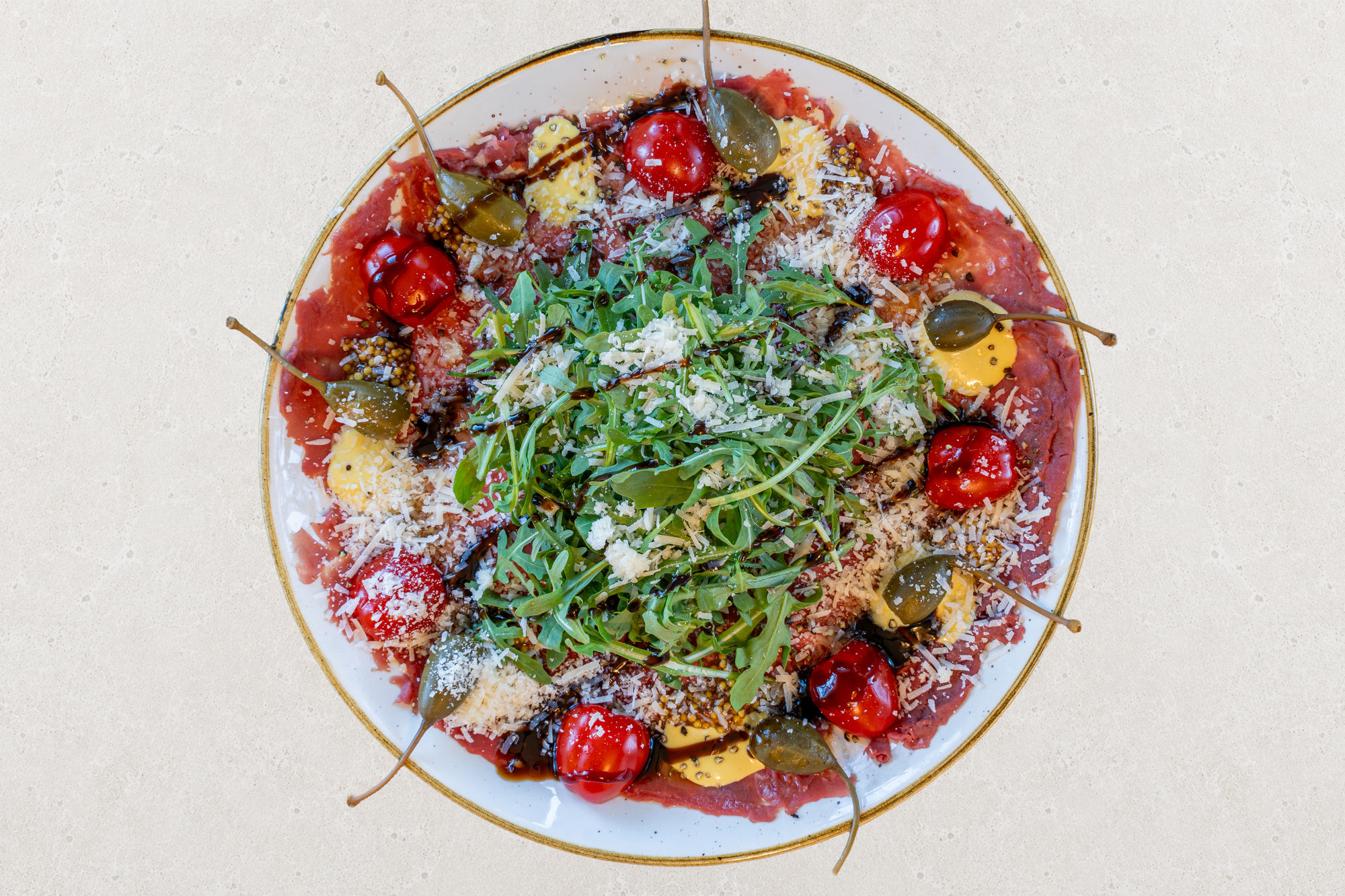 Talerz carpaccio z rukolą, pomidorkami, kaparami i startym serem, polany sosem balsamicznym